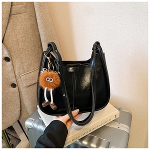 Detail der glänzenden schwarzen Beuteltasche mit niedlichem Plüsch-Anhänger auf Koffer