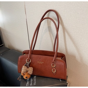 Detalle de bolso vintage de cuero marrón con logo dorado y colgante de oso peluche