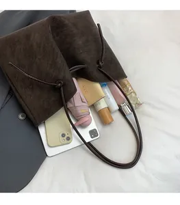 Top view of spacious dark brown suede tote bag filled with a phone, umbrella and cosmetics