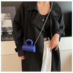 Petit sac cylindrique chic en acrylique avec chaîne dorée sur un manteau noir