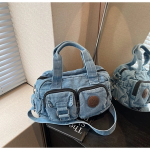 Close-up of denim crossbody bag featuring dual zip pockets and vintage metal buckles