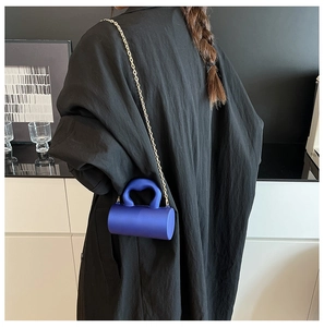 Mini sac cylindrique bleu avec poignée cœur porté par un mannequin en trench noir