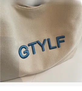 Close-up of light beige canvas tote bag with 3D blue GTYLF embroidery detail
