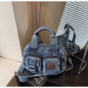 Detail of vintage blue denim crossbody bag with dual front zippers and brown leather logo