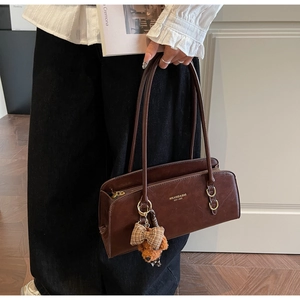 Detalle de bolso bajo el brazo marrón vintage con colgante de oso y letras impresas