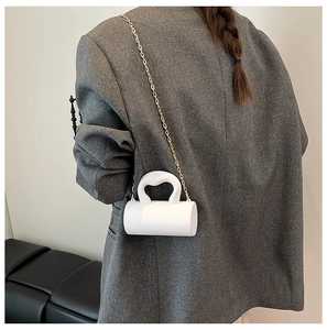 Mini sac cylindrique blanc avec chaîne dorée porté par un mannequin en costume gris