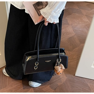 Detalle de bolso negro con grabado dorado y colgante de osito de peluche marrón