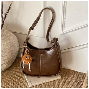 Details der dunkelbraunen halbmondförmigen Tasche mit Pelzanhänger und verstellbarem Riemen