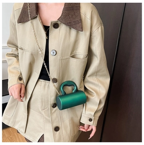 Détail du sac cylindre en acrylique vert émeraude avec chaîne dorée sur tenue beige