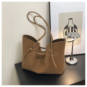 Close-up of brown suede tote bag featuring decorative knots and long thin shoulder straps