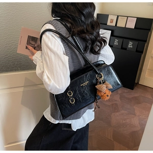 Detalle del bolso de hombro negro brillante con logo dorado y amuleto de osito