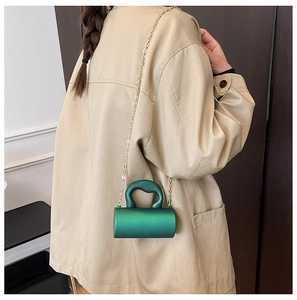 Détail du mini sac cylindrique en acrylique vert avec chaîne en métal doré sur un modèle