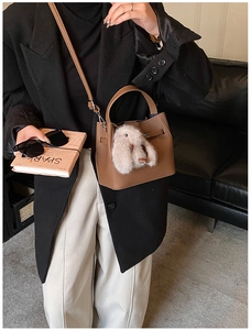 Detail of a brown bucket bag with a plush bunny charm and embossed logo detail