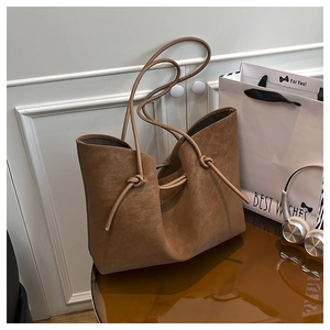 Detailed macro view of brown suede tote bag featuring decorative knot handles and texture