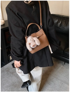 Side view of a brown leather bucket bag featuring a plush rabbit charm on a stylish model