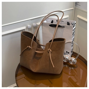 Detail of vintage brown suede tote bag with drawstring knot design on glass table