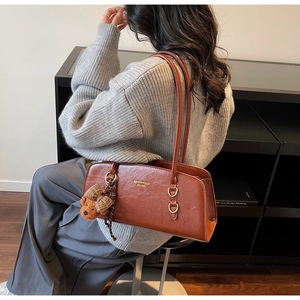 Bolso retro marrón bajo el brazo con textura de cuero y detalle de amuleto de osito