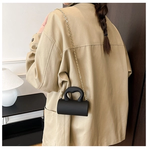 Détail d'un mini sac cylindrique noir avec chaîne dorée sur un mannequin