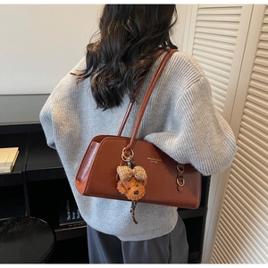 Detalle del bolso de hombro de cuero marrón vintage con dije de oso y logo dorado