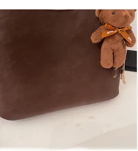 Close-up of textured dark brown tote bag with a cute plush bear charm detail