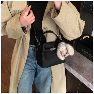 Detail of a black leather bucket bag with silver lock and plush bunny charm accessory