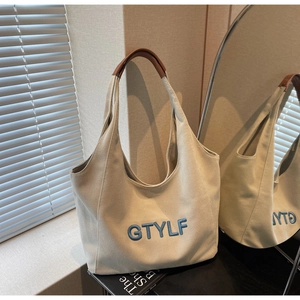 Detail of cream canvas tote bag with blue GTYLF embroidery and brown leather handles