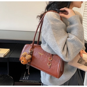 Detalle del bolso de hombro en cuero marrón vintage con charm de oso y logotipo oro
