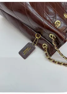 Detail der braunen gesteppten Lederstruktur mit Goldkette und Markenanhänger