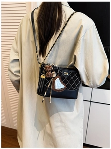 Detail of black quilted crossbody bag with golden chain strap and decorative charms