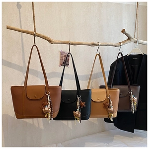 Detail of minimalist tote bags in four colors hanging on a wooden branch with bear charms