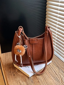 Braune Vintage Eimertasche mit Plüsch-Monster-Anhänger auf Holztisch bei Sonnenlicht