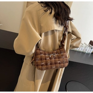 Detail of a brown plaid underarm bag with a metallic bow and scrunchie leather strap