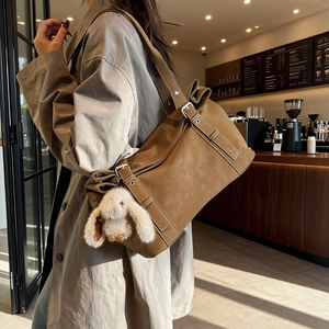 Brown matte tote bag with plush bunny charm worn by model in a cozy cafe setting