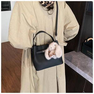 Detail of black pebbled leather bucket bag with metal buckle and plush bunny charm
