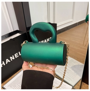 Détail du sac cylindrique vert foncé avec poignée cœur dorée et fine chaîne en métal