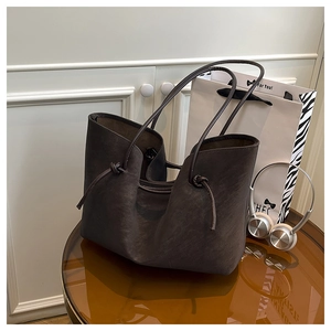 Detail of dark brown matte leather tote bag featuring unique knotted strap side accents