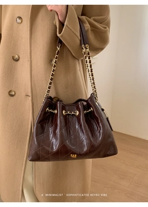 Detail einer Vintage-Steppleder-Eimertasche in Dunkelbraun mit goldenem Kettenriemen