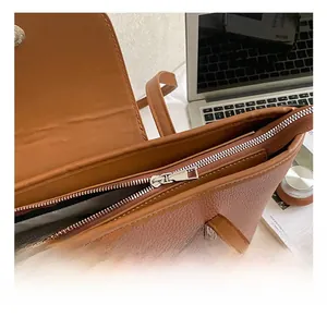 Detailed close-up of metallic zipper and magnetic snap on a brown pebbled tote bag