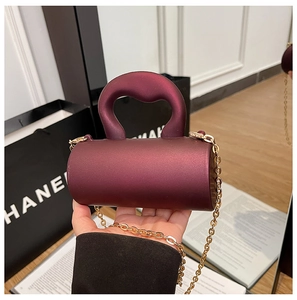 Détail du mini sac cylindre bordeaux mat avec bandoulière chaîne dorée tenu à la main