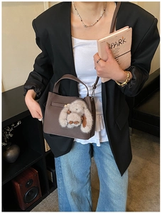 Detailed shot of brown pebble leather bucket bag with a plush bunny charm on a model