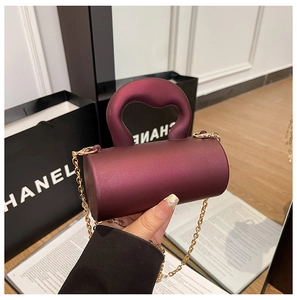 Détail d'un mini sac cylindrique bordeaux avec texture mate et fine bandoulière dorée
