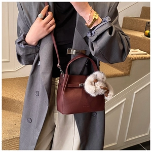 Detail of dark red pebbled leather bucket bag with metal clasp and grey plush rabbit charm