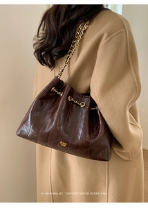 Detail der dunkelbraunen gesteppten Hobo-Tasche mit Goldkette auf einem Wollmantel