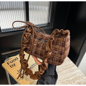 Detailed shot of brown plaid handbag with silver bow charm and ruffled handle design