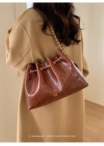 Braune gesteppte Beuteltasche mit Goldkette, präsentiert von einem Model im Mantel