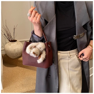 Close-up of burgundy leather bucket bag with brand logo and soft plush doll pendant