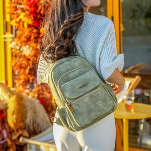 Detail of green suede backpack showing metal JINGPIN logo and zippers in outdoor setting