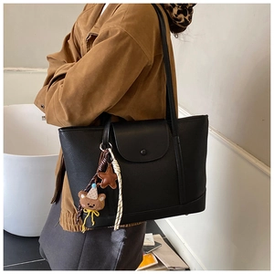 Detail of black pebbled leather tote bag with side bear charm and shoulder straps