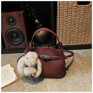Detail of burgundy bucket bag featuring pebbled texture, metal lock and cute bunny charm