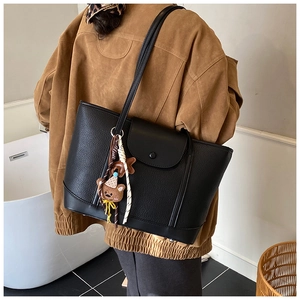 Black pebbled leather tote bag shown on shoulder with a cute brown bear charm